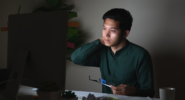 Male student considering financial fit in choosing his college by researching costs on his computer.