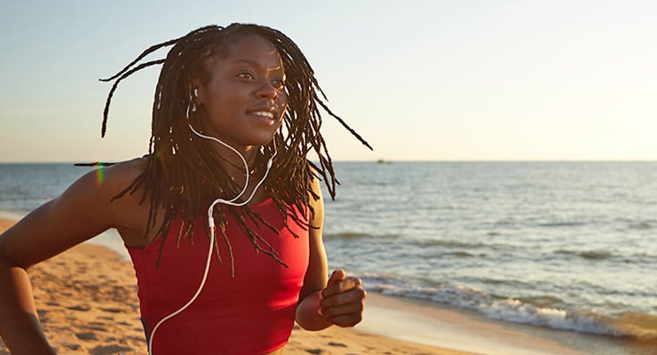 Female student running and listening to music on the beach to reduce stress.