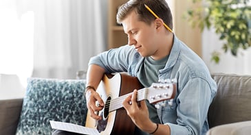 Mężczyzna student gra na gitarze, aby zmniejszyć stres.