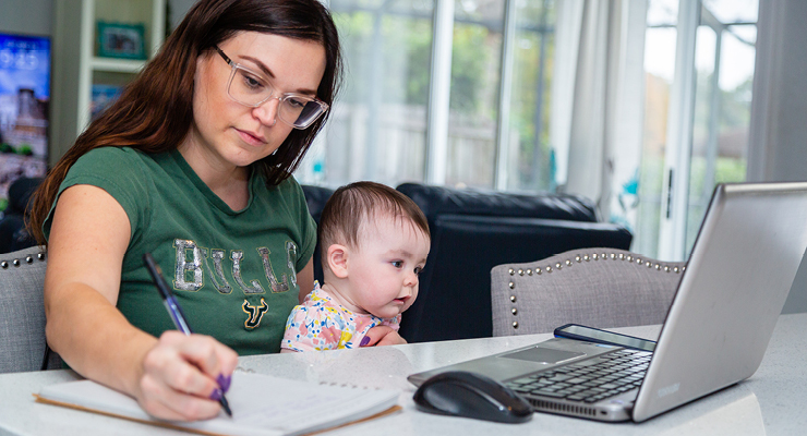 A nontraditional student who is a parent sitting at home with a baby doing school work.