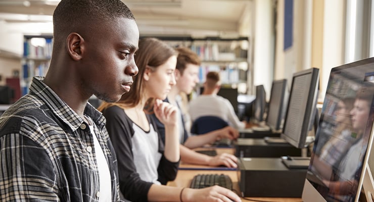 An African American student sitting in front of a computer search for colleges