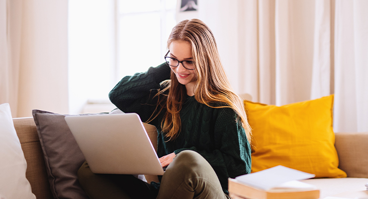 A female college students sitting on a couch with her laptop completing a transfer student application.