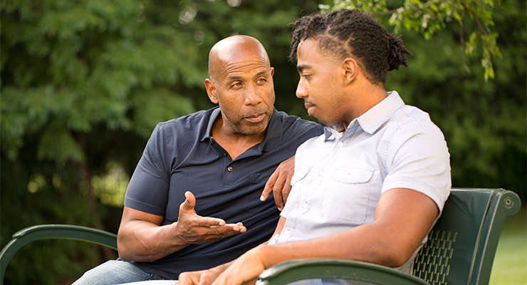 Father and son sitting outdoors having a conversation.