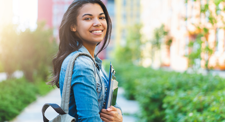 A female student carrying her school supplies and smiling.