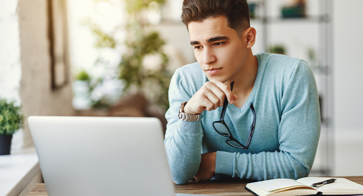 Male in a blue shirt looking at his laptop trying to figure out how to minimize college debt