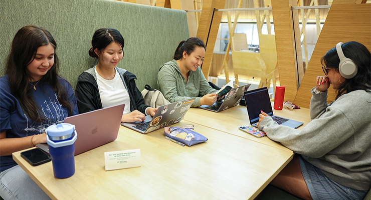 A group of four USF students sitting around a table with laptops at the Judy Genshaft Honors College