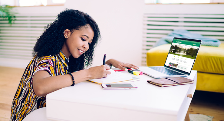 Female student researching the reasons to finish high school strong on her laptop and writing notes.