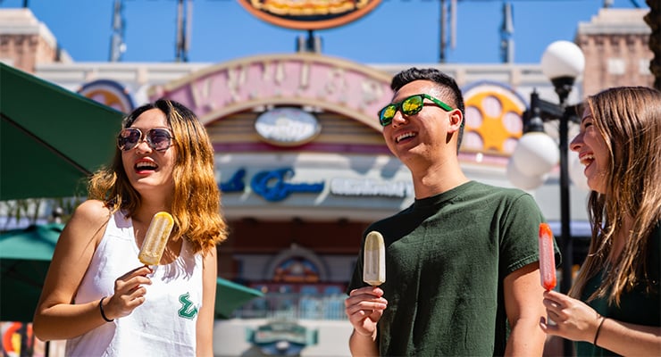 Three USF students eating popsicles outside.