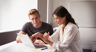 A young man and a woman looking and pointing at the screen of a laptop.