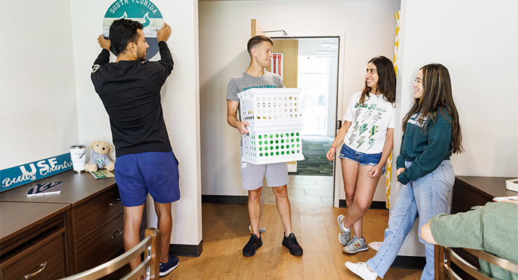 Four students chatting while setting up their dorm room.