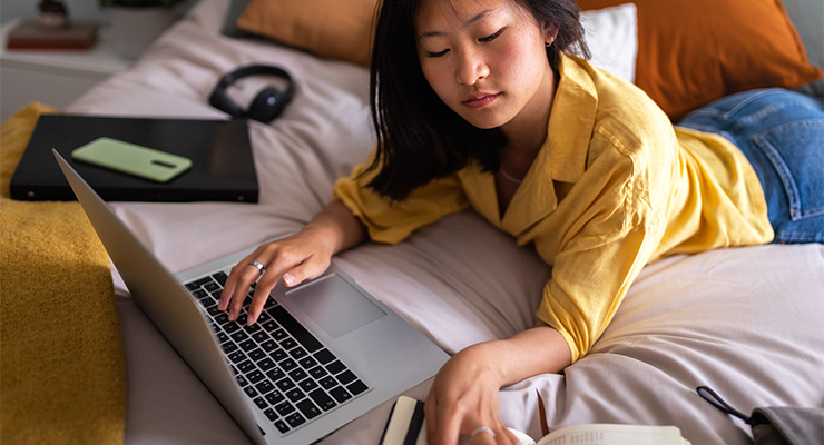 A student studying in her dorm on the bed.