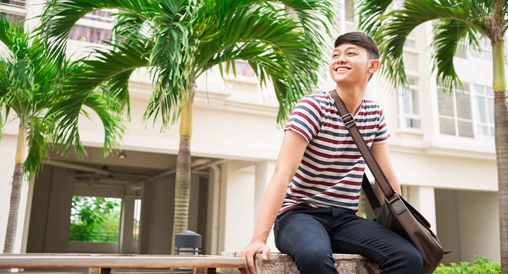 A student smiling and sitting on a bench on campus.
