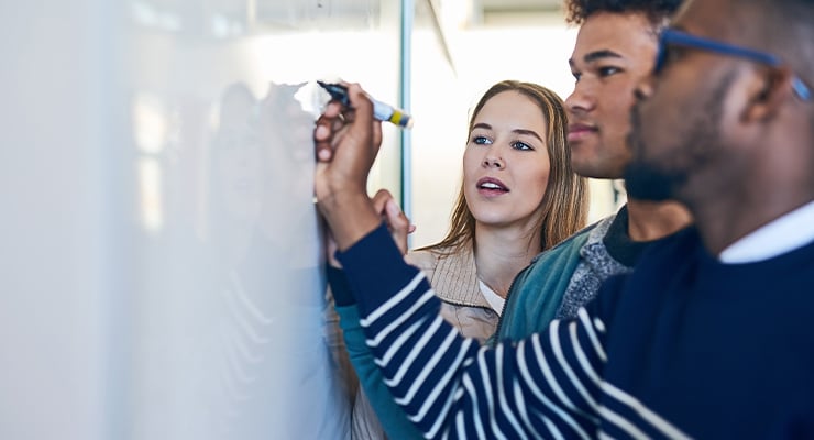 College counselor writing on a whiteboard while helping students.