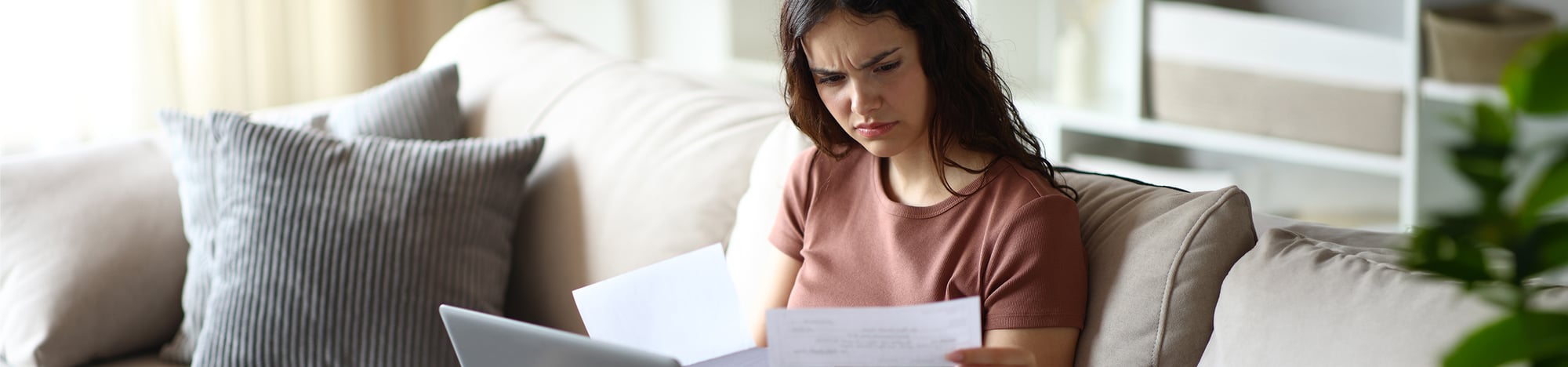 A student sitting on a couch at home while reviewing documents.