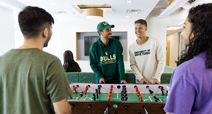A group of friends playing foosball in their dorm hall.