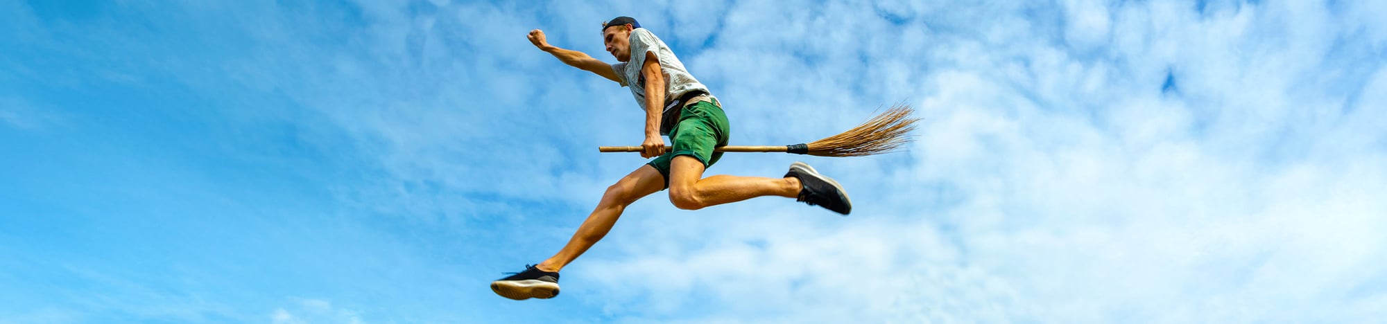 A man flying mid-air on a broom.