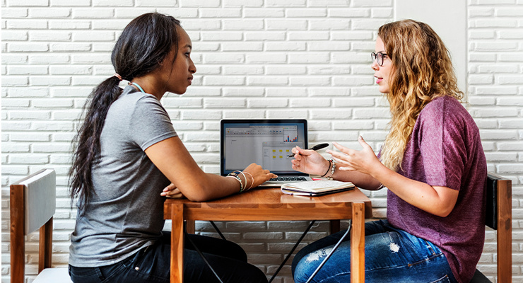 Two students sitting together at a table and collaborating on a project.