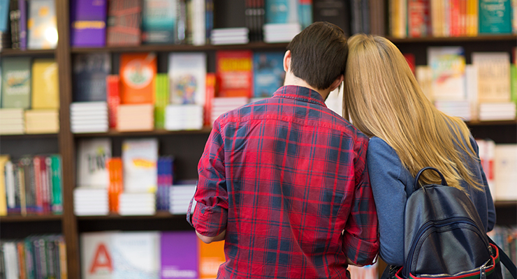 A man and a woman pressing their heads against each other in a library.
