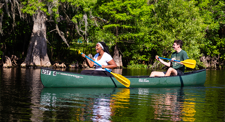 A man and a woman happily canoeing on water.