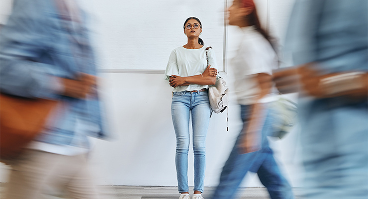 Student standing in the background with students moving in front of her.