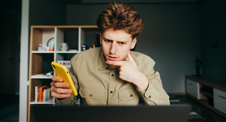 A guy holding his phone while doing some research on scholarship scams.