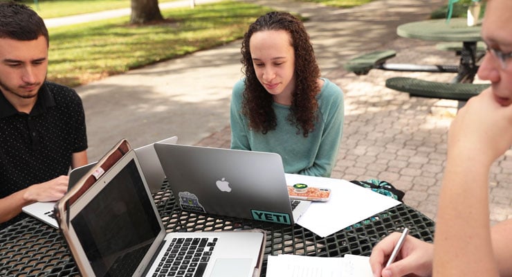 Three USF students study at a table on campus outside.