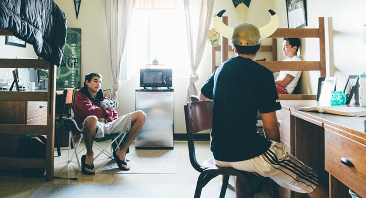 Three USF students talk to each other in a residence hall room.