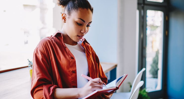 An female high school student writes makes notes to help her college decision