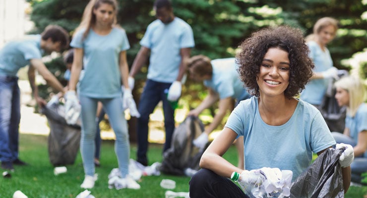 A group of college students in matching blue shirts picking up trash in the park