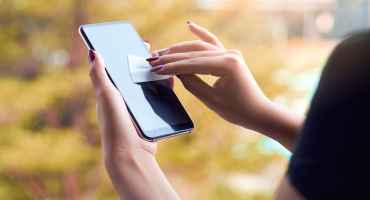 A woman cleans the screen of her smart phone with disposable wipe