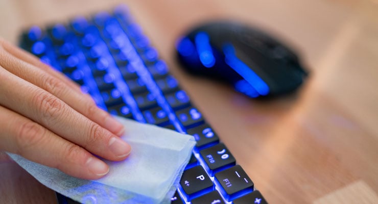 A man cleans his keyboard with a disposable wipe