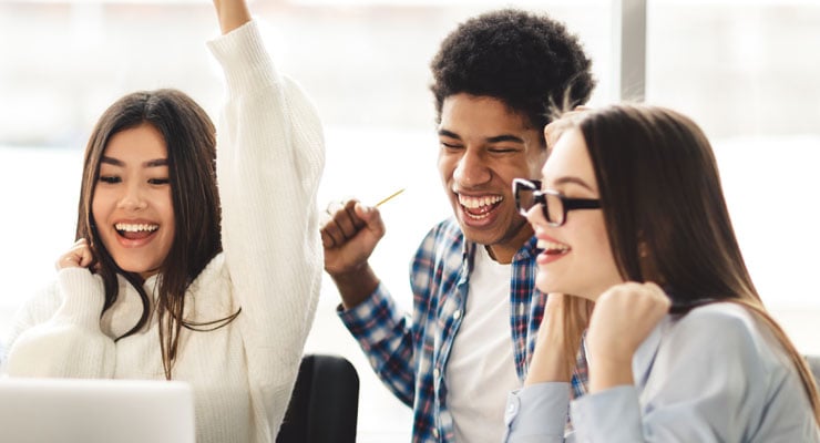 A group of three students gather around a laptop and celebrate good news