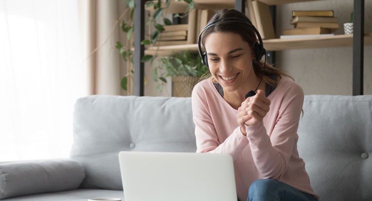 A female student sits on her couch at home while teleconferencing with her college counselor on a laptop