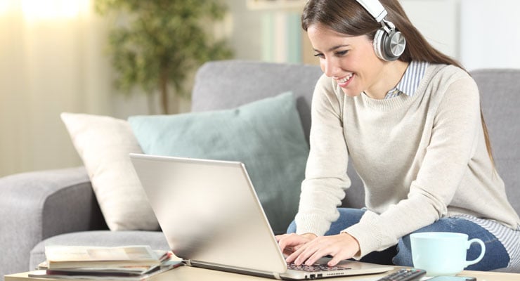  A female student in a beige sweater with headphones attends a online course on her laptop