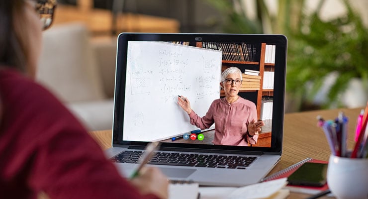 Student takes notes while watching an online class on her laptop computer