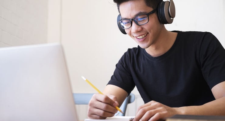 Male student in a black t-shirt wearing headphones while working in front of his laptop