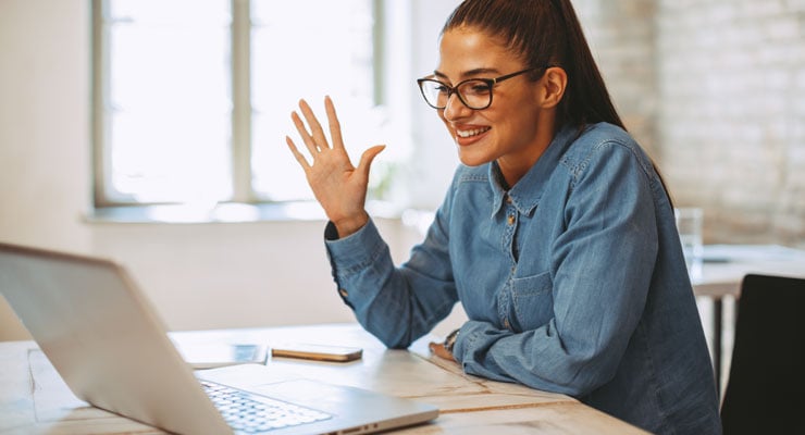 A female student raises her hand and waits to be called on in her online class