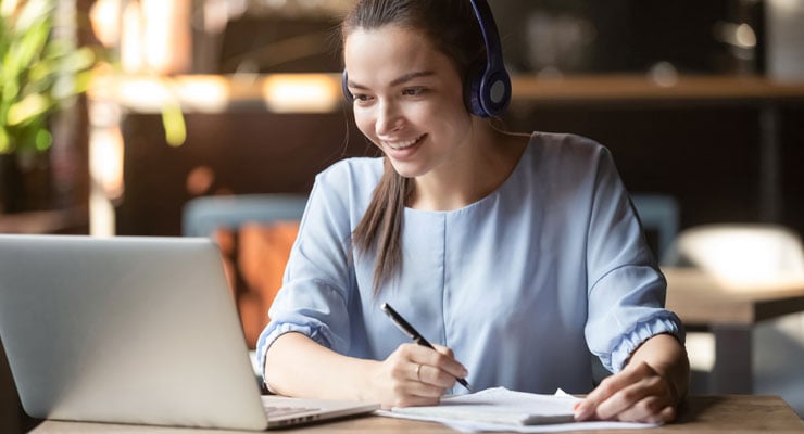 caucasian female student taking notes on her laptop for an online course