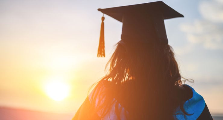 A student in academic regalia watches the sun set and contemplates whether she is ready for college.