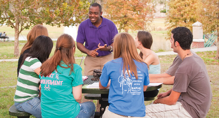 Group of students sitting at a table listening to a mentor speak