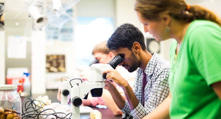 Science students use microscopes and their professor provides instruction