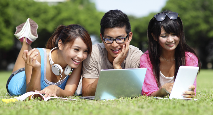 Three students sitting outside talking about applying to college and looking at tablets.