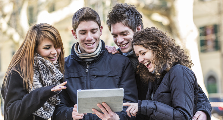 Four students looking at a tablet and smiling.