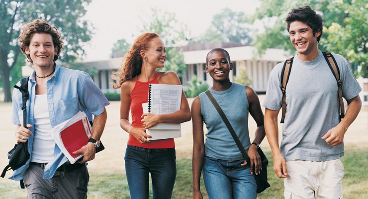 A group of four high school students with books walk together and smile.