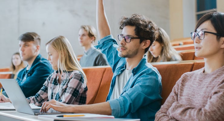 College student raises his hand to ask a question in a college classroom.