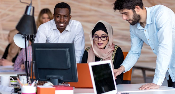 Three college students work on a computer together.