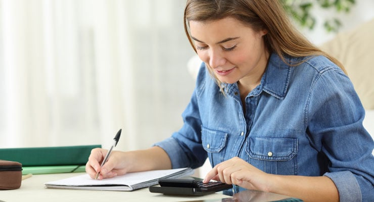 Female student improving her college cash flow by calculating her expenses with a calculator and notebook.