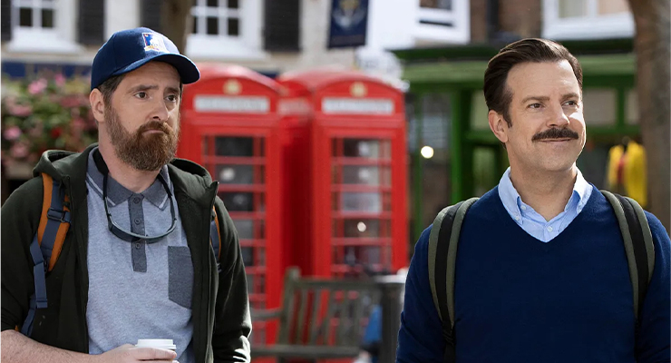 Ted Lasso and Coach Beard standing in front of two telephone booths. 