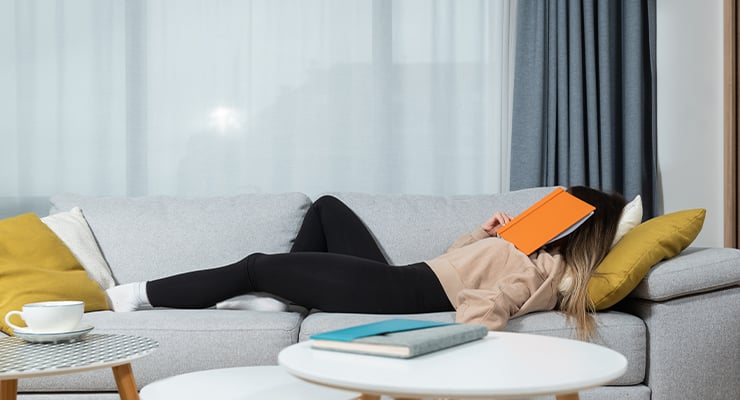 A student lying on the coach with an orange book on her face.