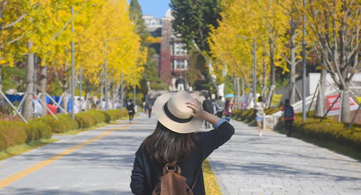 A student touching her hat while walking on campus.